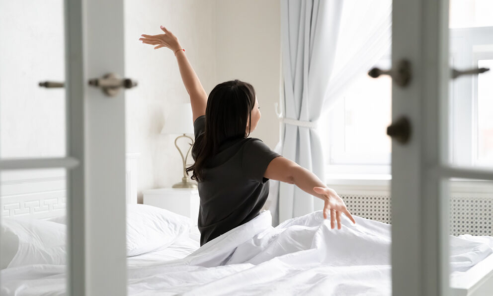A woman stretching as she sits up in bed
