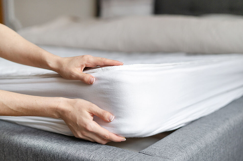 A pair of hands holding a mattress on a bed